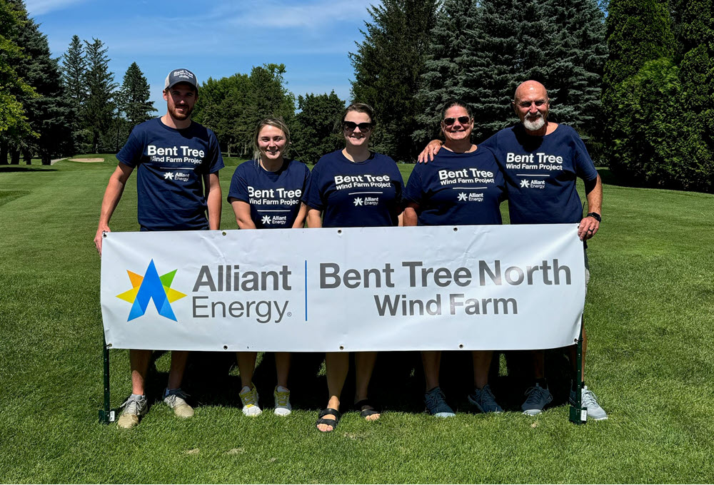 Five people standing behind a Bent Tree North Wind Farm sign