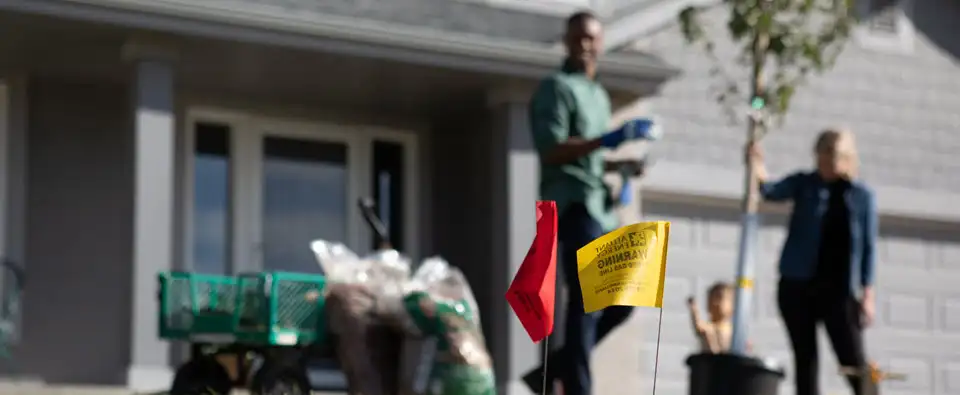 Couple planting tree with utility flags in yard